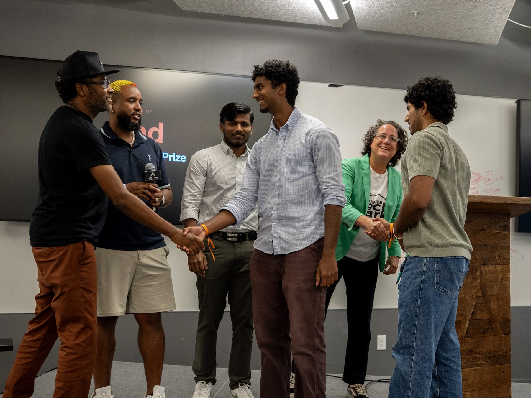 Hackathon organizers shaking hands with winning team members on stage at Atlanta Tech Village