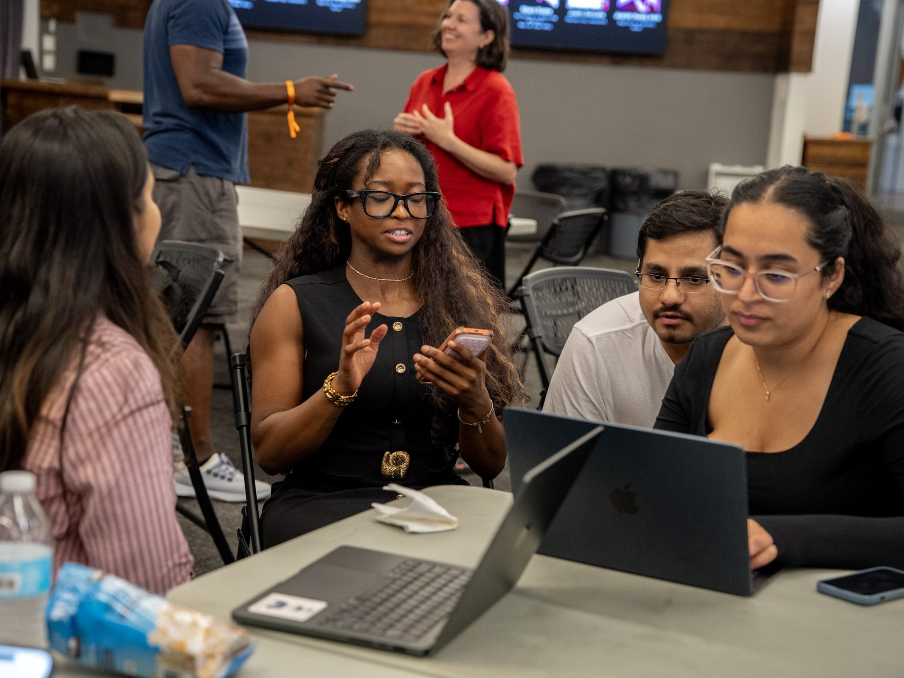 Hackathon participants collaborating around laptops and phones